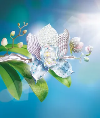 Glass orchid sculpture on a branch with green leaves under bright sunlight by Tom Krieger