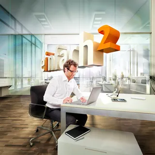 Man working on laptop in office with Arch2D logo floating, artwork by Tom Krieger