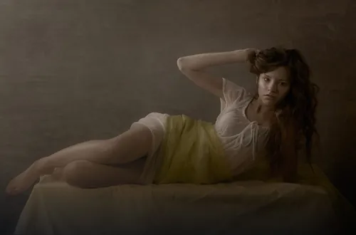 Woman reclining on bed in soft lighting by Tom Krieger