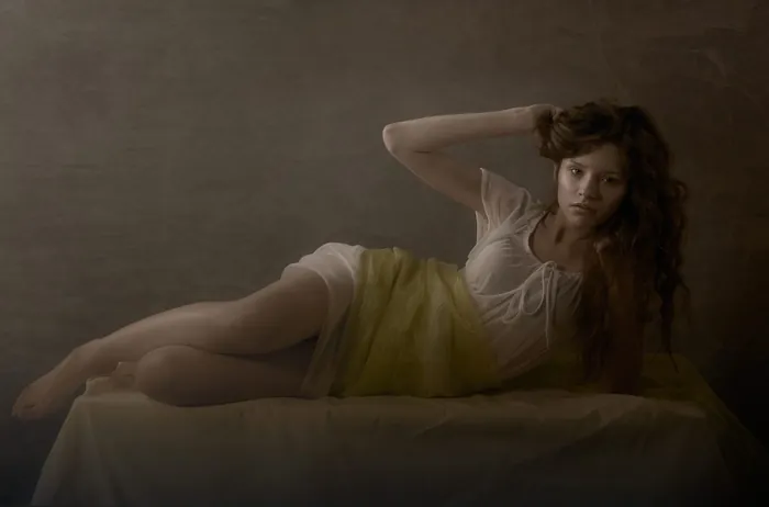 Woman reclining on bed in soft lighting by Tom Krieger
