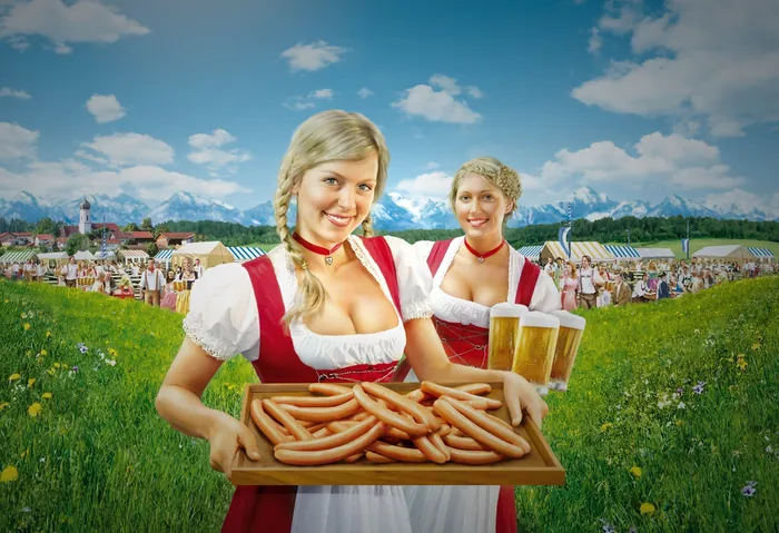 Two women in traditional dress holding sausages and beers outdoors by mountains, artwork by Tom Krie
