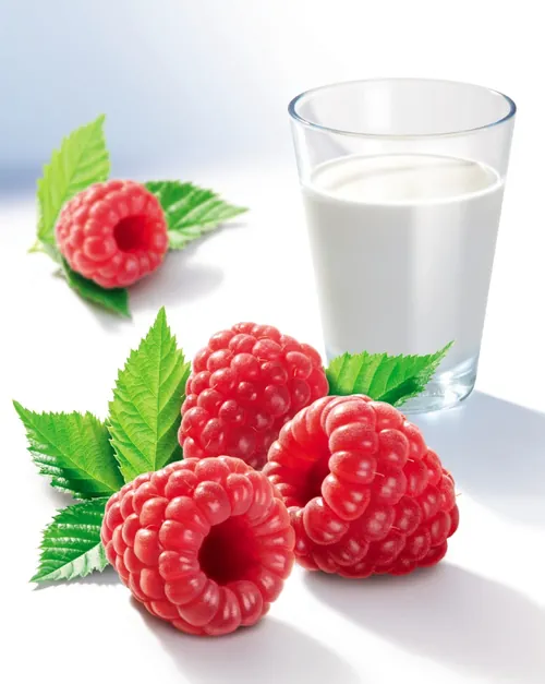 Glass of milk with three fresh raspberries and green leaves by Tom Ungemach