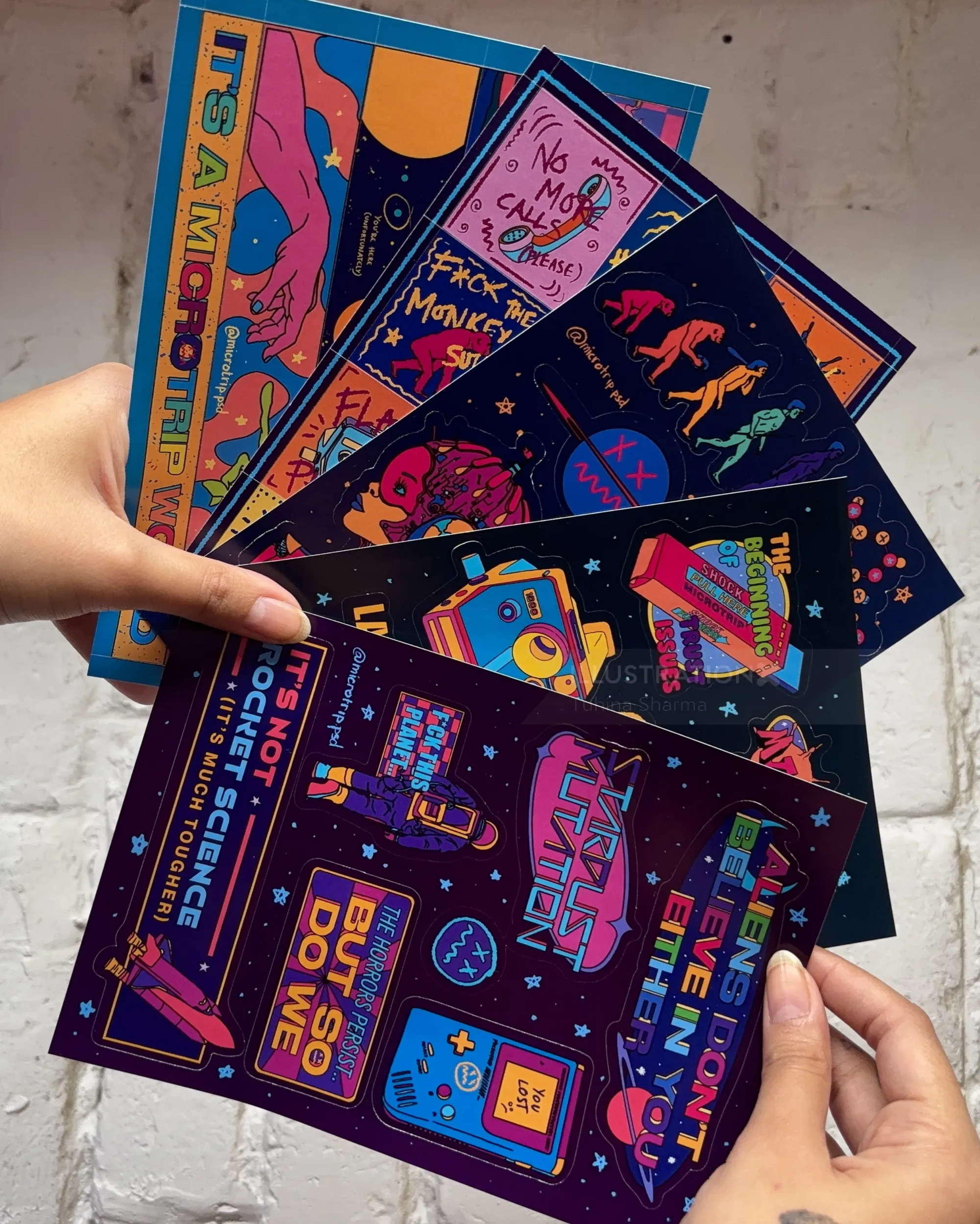 Colorful illustrated posters held by a hand showcasing diverse creative designs by Tuhina Sharma