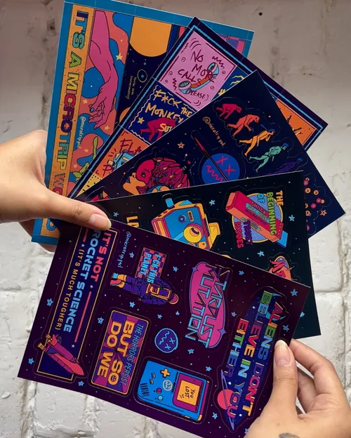 Colorful illustrated posters held by a hand showcasing diverse creative designs by Tuhina Sharma