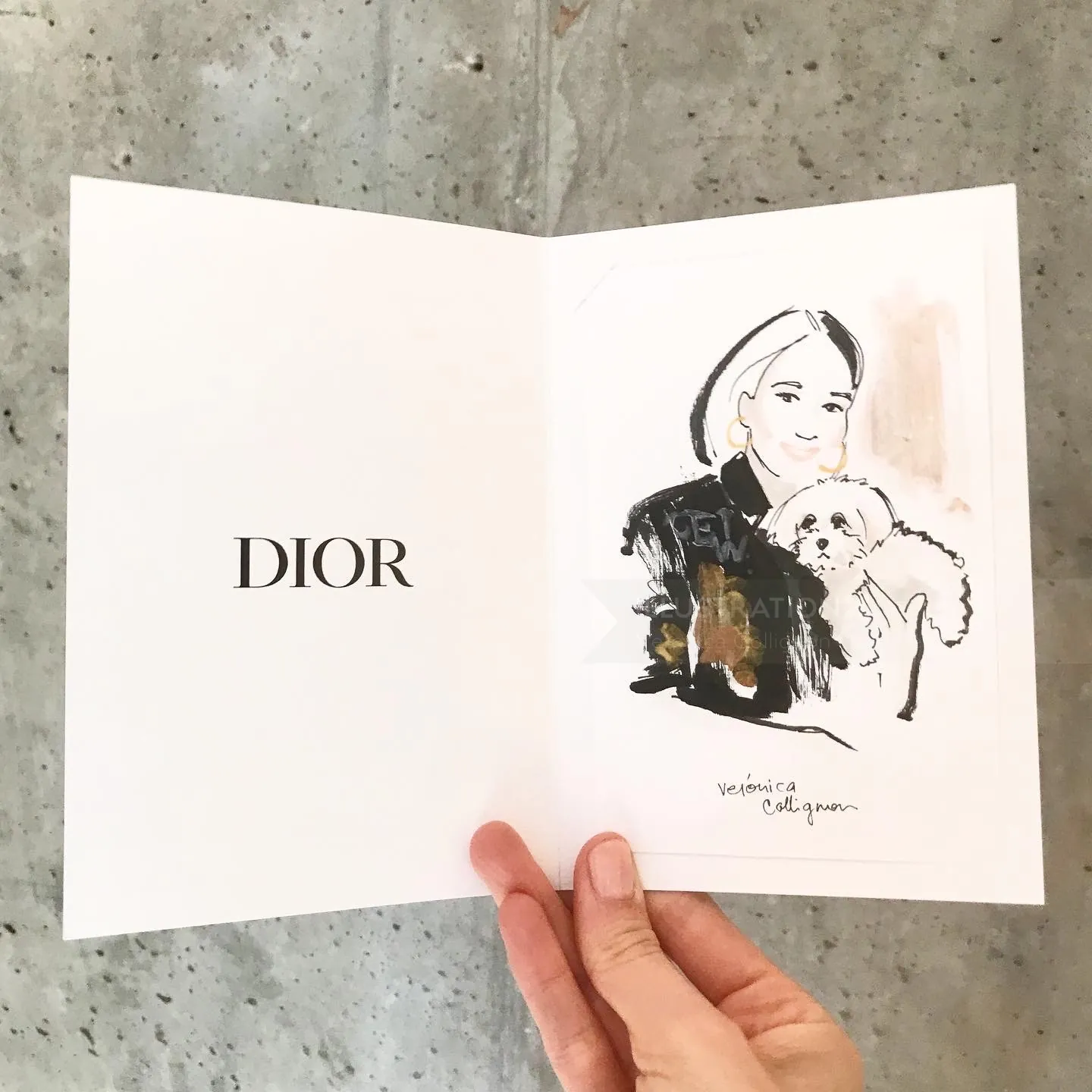 Main tenant une carte Dior avec un croquis de femme et de chien par Veronica Collignon