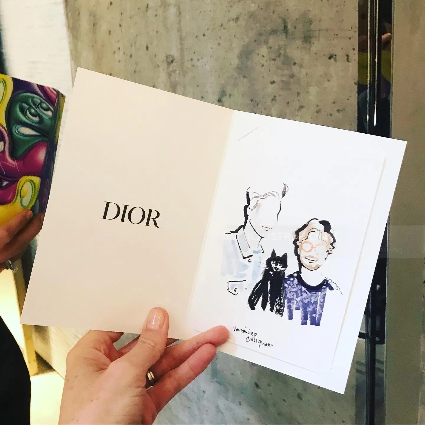 Hand holding Dior card with minimalist fashion sketch by Veronica Collignon