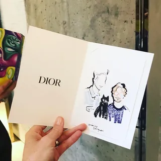 Hand holding Dior card with minimalist fashion sketch by Veronica Collignon