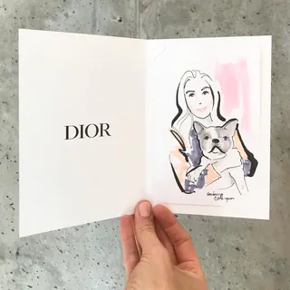 Watercolor illustration of woman holding dog inside Dior card by Veronica Collignon