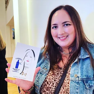 Smiling woman holding a minimalist portrait with a blue bottle by Veronica Collignon