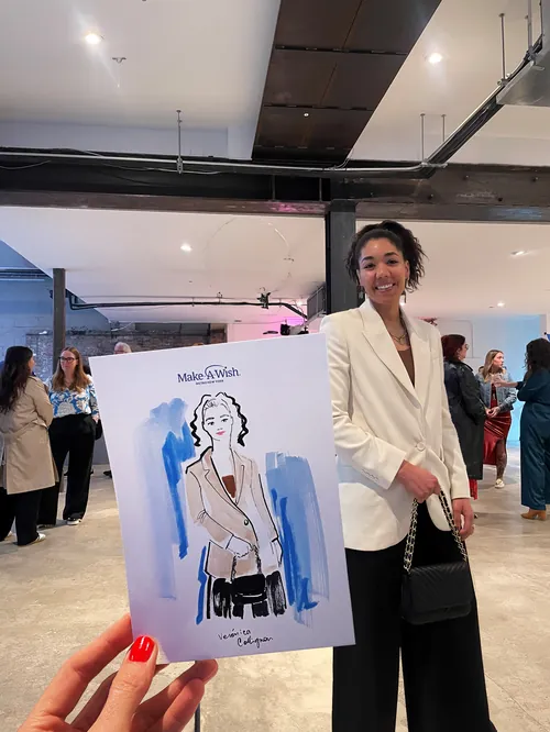 Hand holding fashion sketch of woman in blazer in gallery with attendees