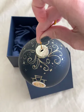 Hand holding navy blue Christmas ornament with gold intricate design