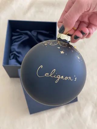 Hand holding black Celignon's Christmas ornament with gold lettering