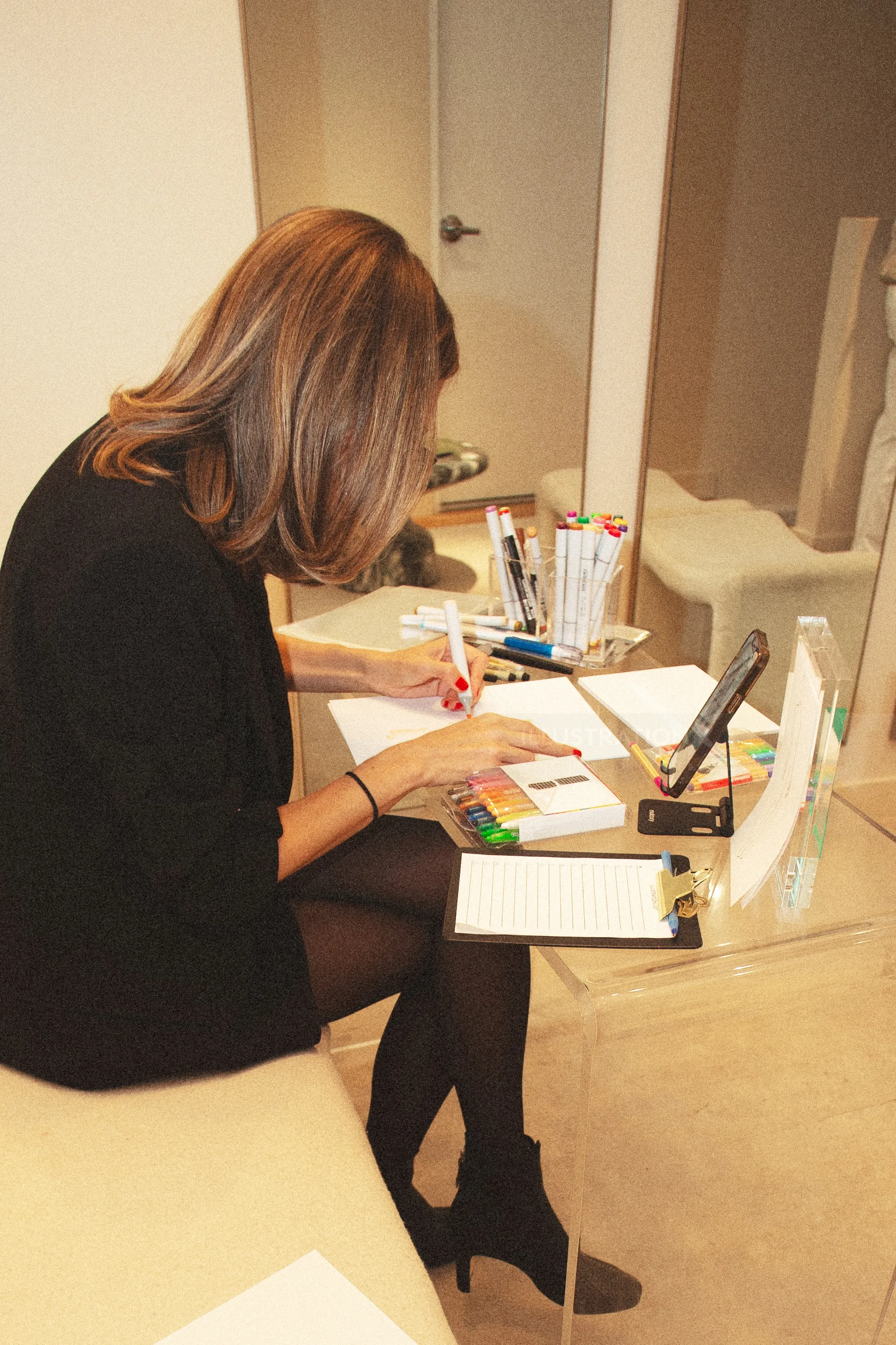 Woman writing notes at desk with pens, notebook, and tablet