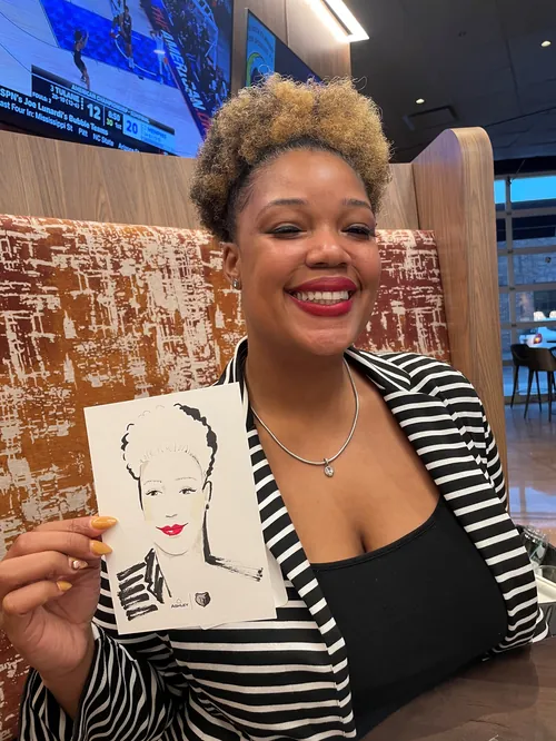 Woman smiling and holding a portrait sketch in a cafe