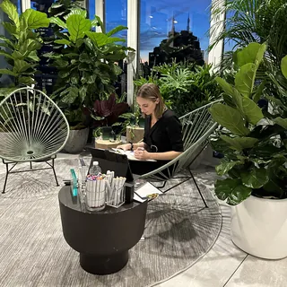 Woman seated in plant-filled lounge working on laptop at night