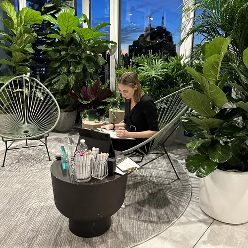 Woman seated in plant-filled lounge working on laptop at night