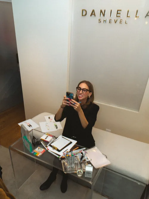 Smiling woman with glasses sitting on bench using phone in office.