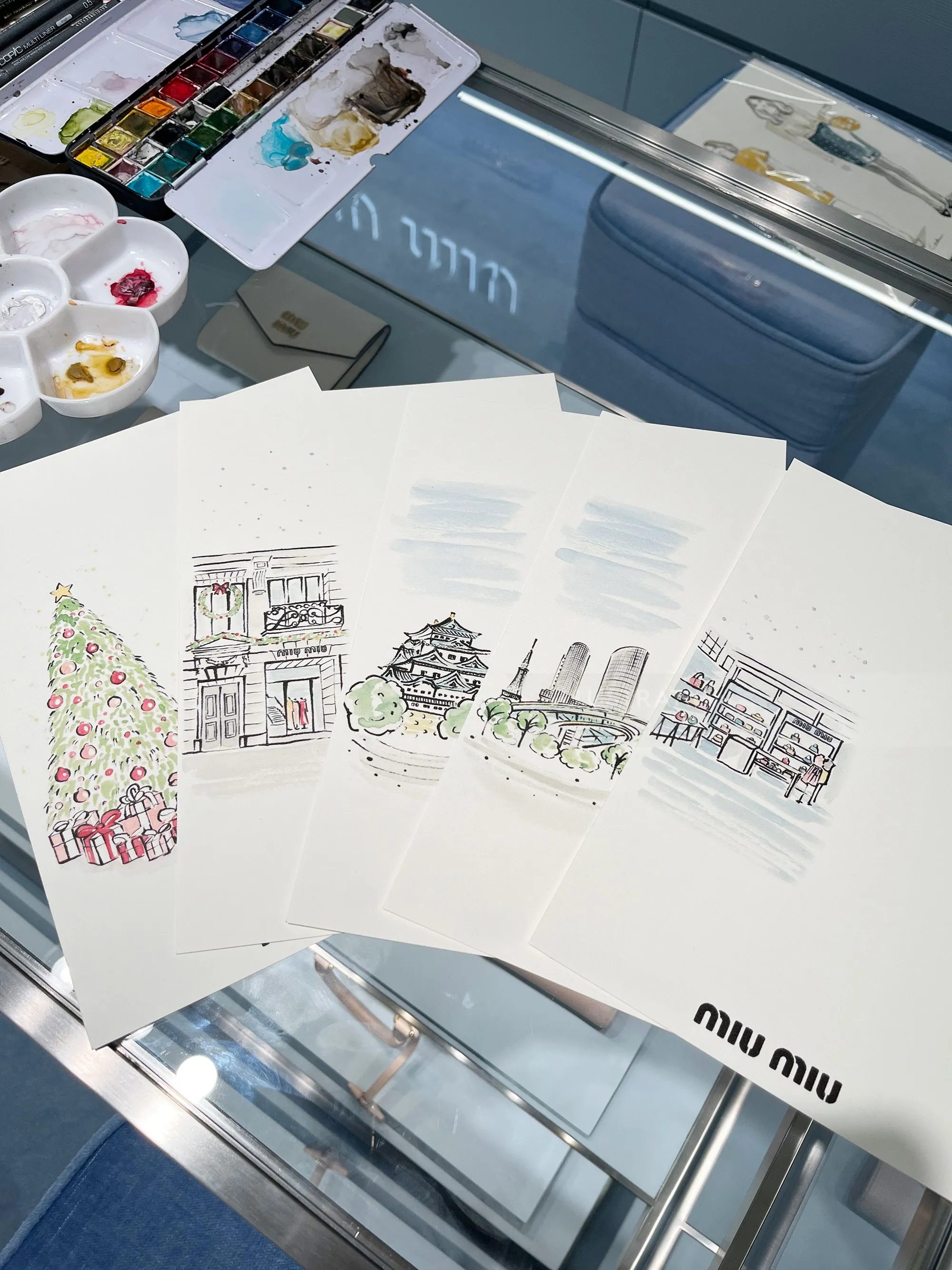 Watercolor sketches of buildings and a Christmas tree on table