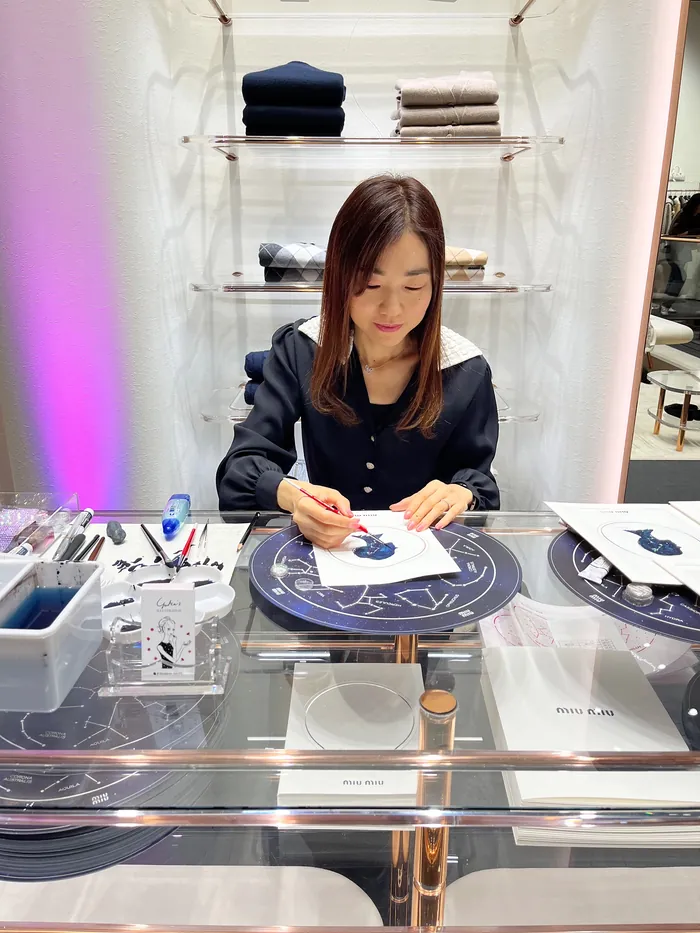 Woman drawing at a table during a MIU MIU live event