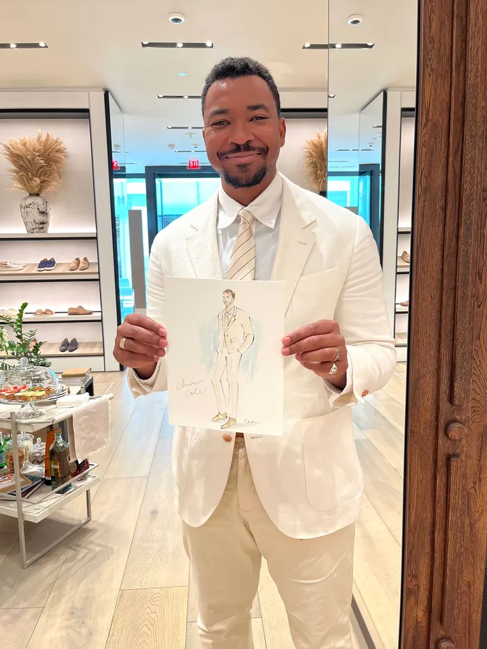 Man in white suit holding fashion sketch in boutique