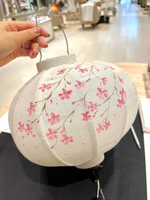 Hand holding white lantern with pink floral pattern indoors