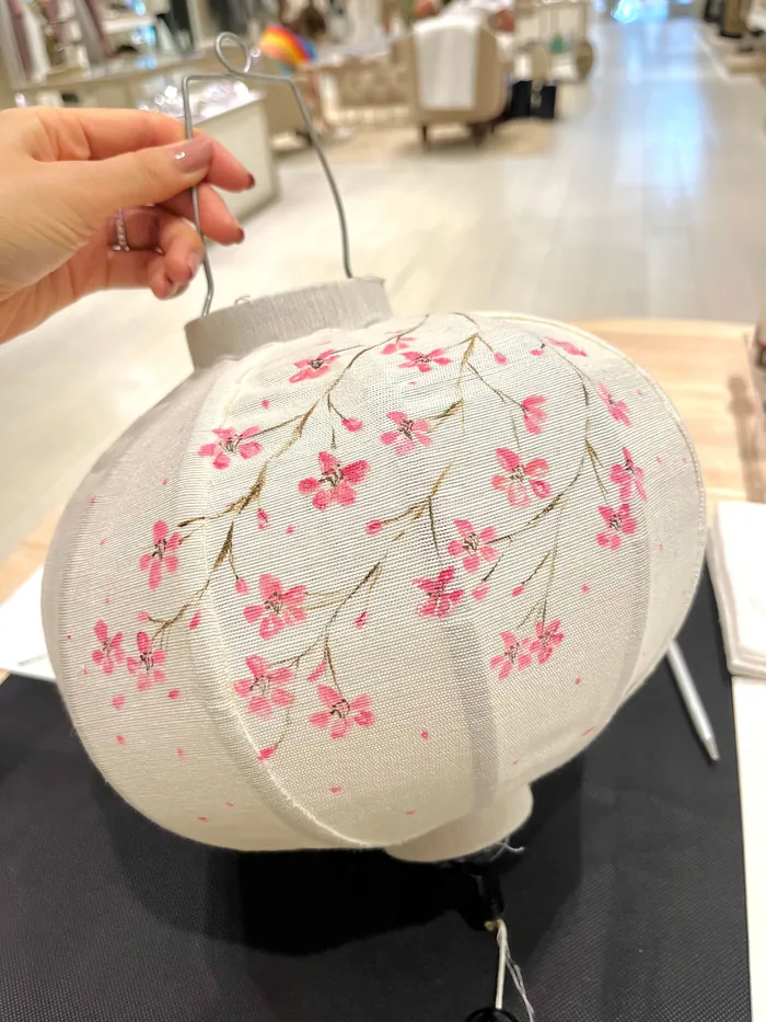 Hand holding white lantern with pink floral pattern indoors