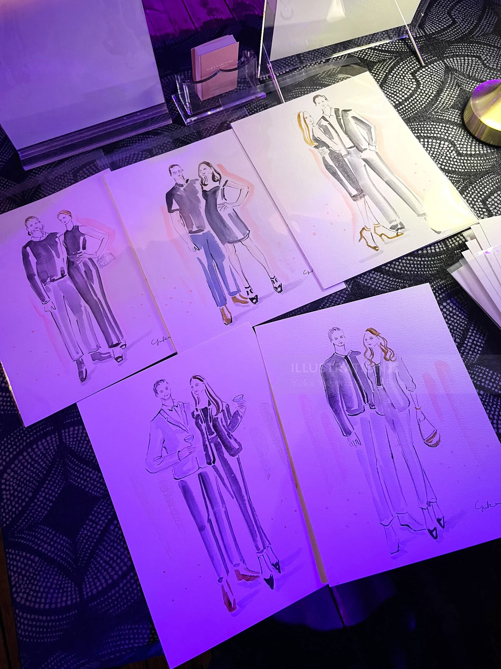 Fashion sketches of male and female models on table under purple light