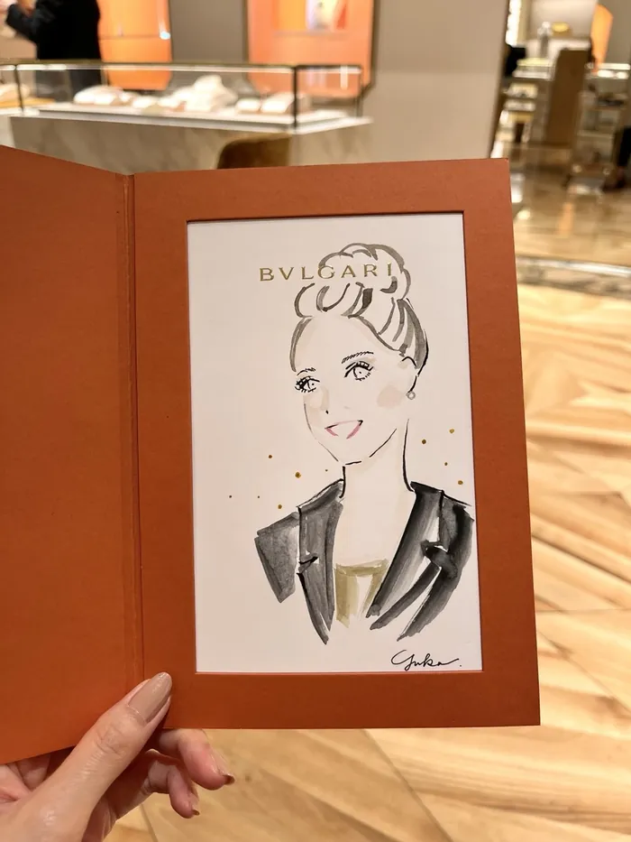 Hand holding a sketch of a woman in a Bulgari frame at an event