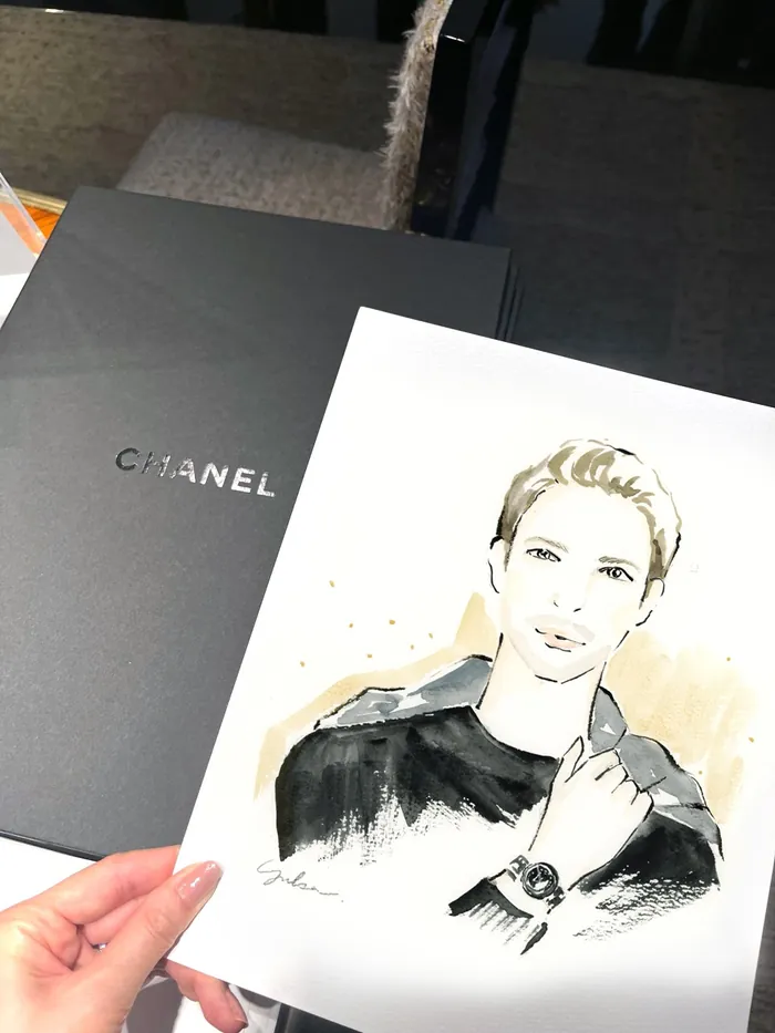 Hand holding a sketch of a person with Chanel box in background