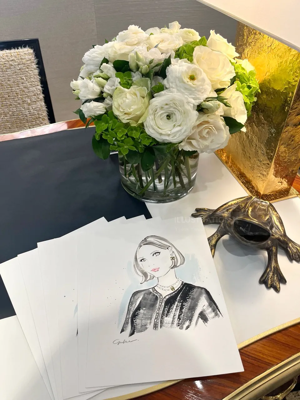 White floral bouquet next to fashion illustration sketches and a decorative frog