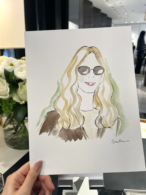 Hand holding a watercolor portrait of a woman with sunglasses