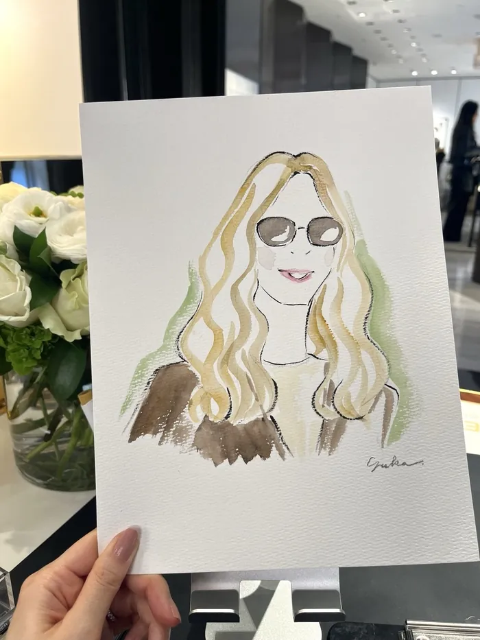 Hand holding a watercolor portrait of a woman with sunglasses