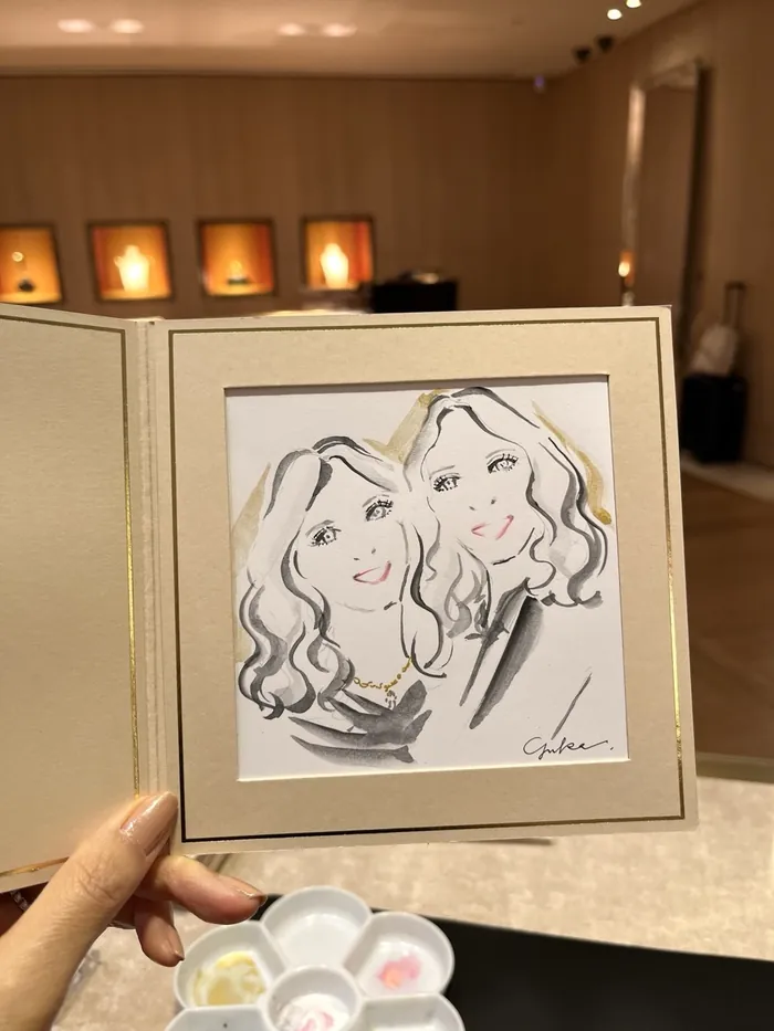Hand holding a caricature drawing of two women at an indoor event