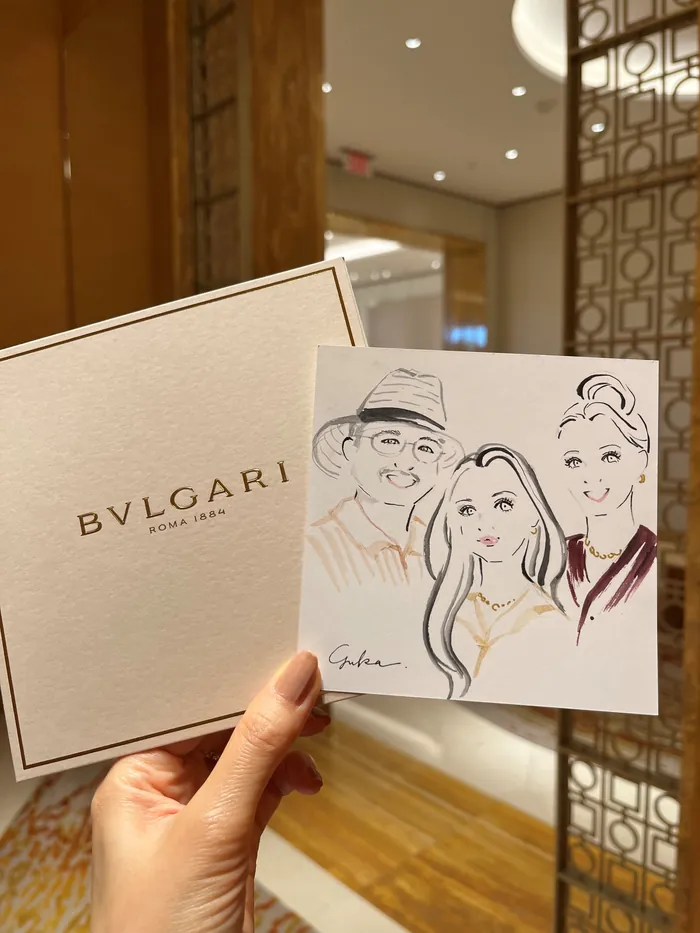 Hand holding a Bvlgari box and a sketch of three people