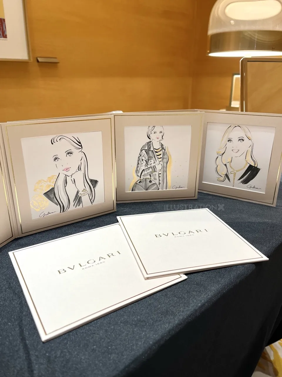 Illustrations of women in fashion with Bulgari branded cards on table