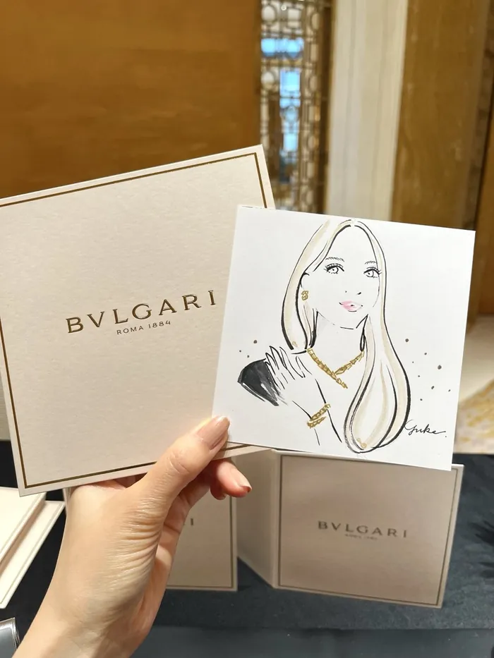 Hand holding illustrated portrait with Bulgari packaging in background