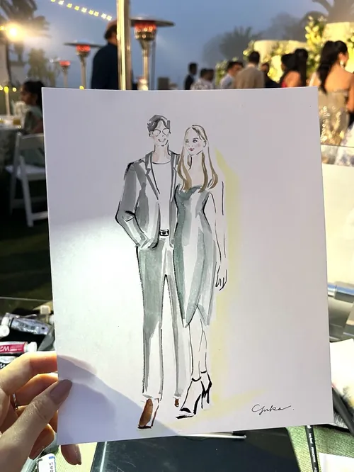 Hand holding a stylish sketch of a man and woman at an outdoor event