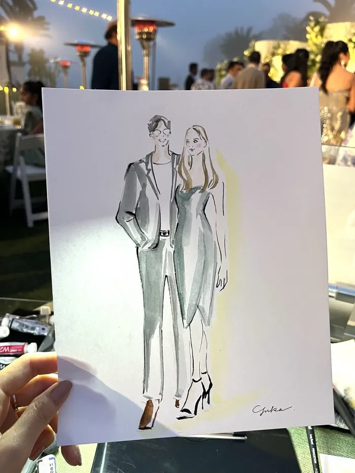 Hand holding a stylish sketch of a man and woman at an outdoor event
