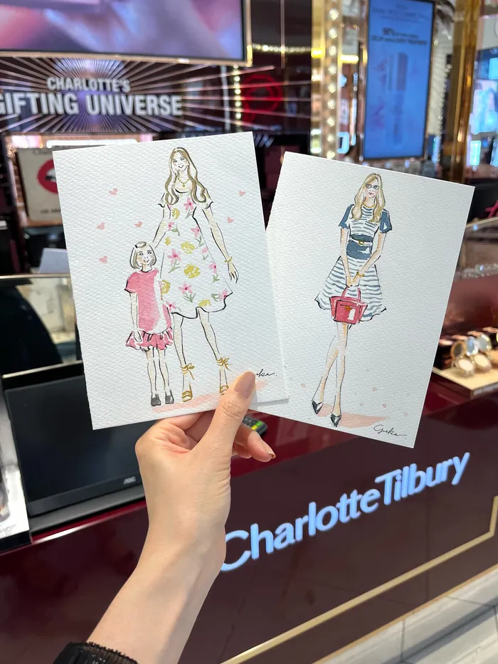 Hand holding two fashion illustration sketches at Charlotte Tilbury event