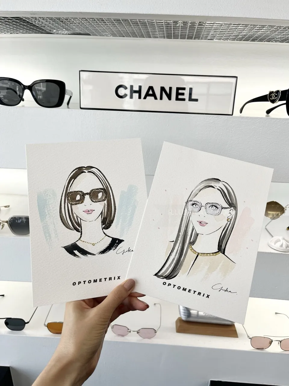 Hand holding illustrations of women wearing glasses in optical store