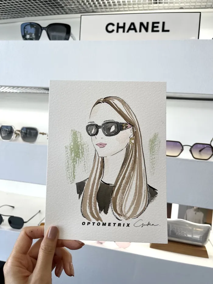 Hand holding illustration of woman wearing sunglasses in optometry store