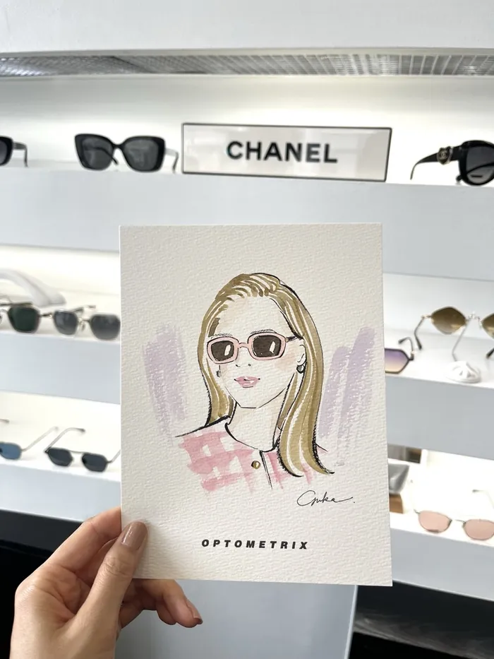 Hand holding illustration of woman wearing sunglasses in eyewear store
