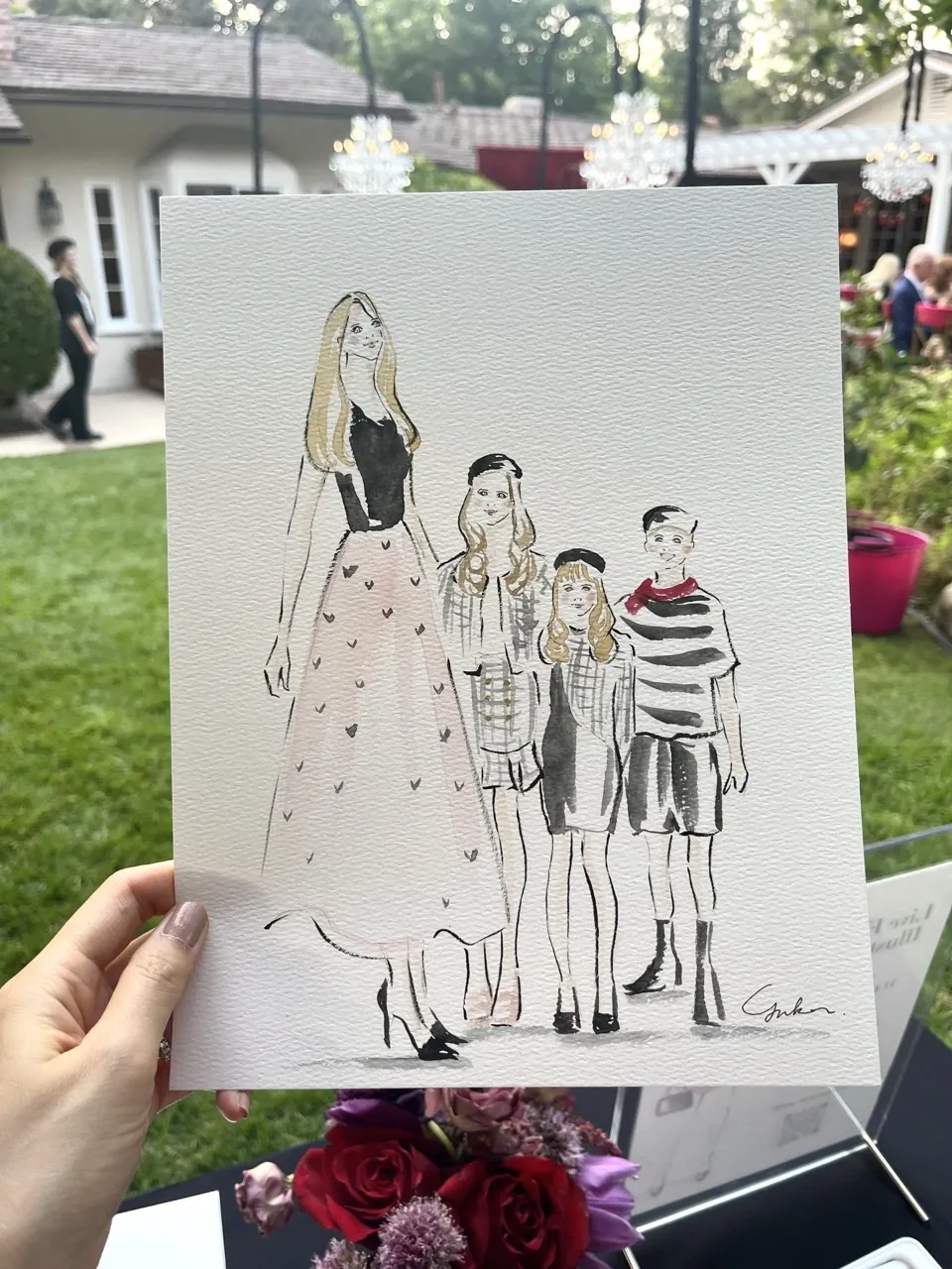 Hand holding fashion illustration of four people at outdoor event