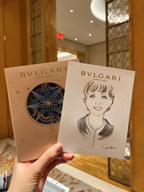 Hand holding Bulgari event card and portrait drawing by Yuka Yasutomi