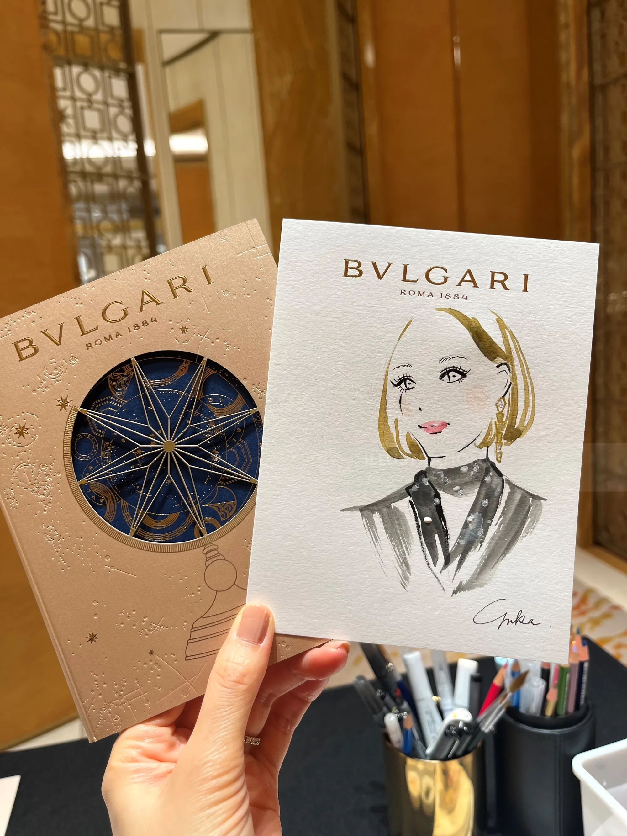 Hand holding Bulgari event cards with fashion illustration by Yuka Yasutomi