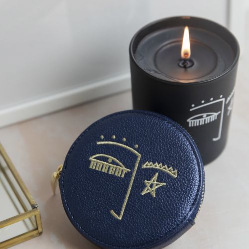 Navy blue pouch with abstract face illustration beside lit black candle.