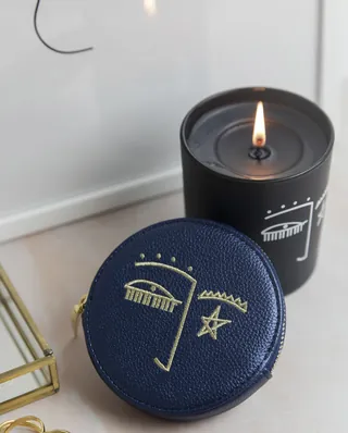 Navy blue pouch with abstract face illustration beside lit black candle.