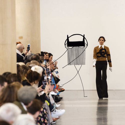 Fashion model walking on runway at fashion show with audience taking pictures