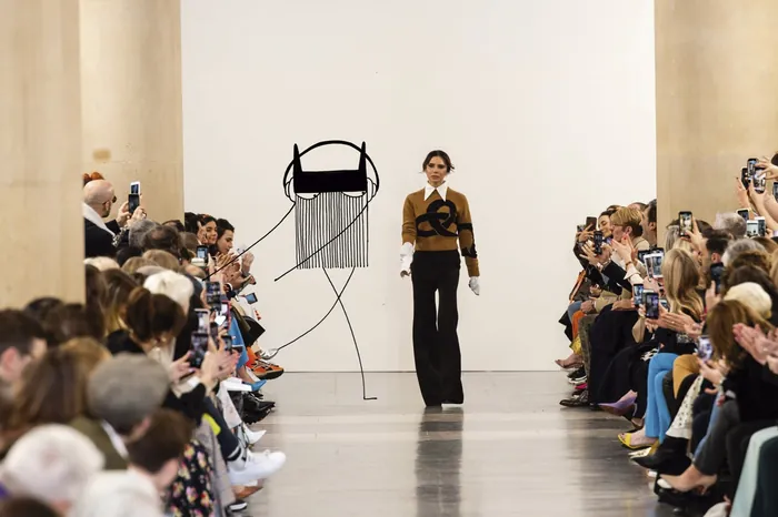 Fashion model walking on runway at fashion show with audience taking pictures
