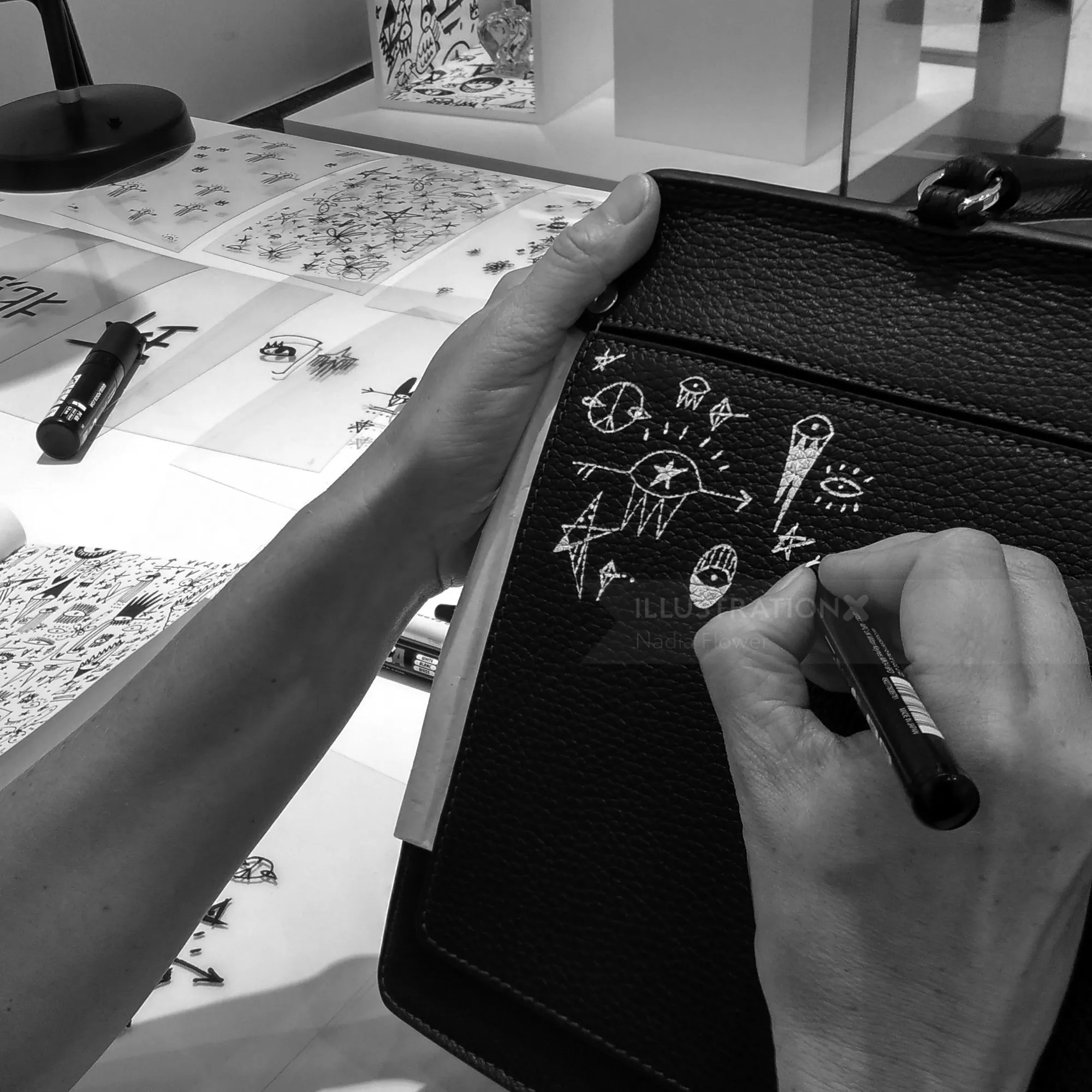 Hands creating white abstract doodles on black leather with marker